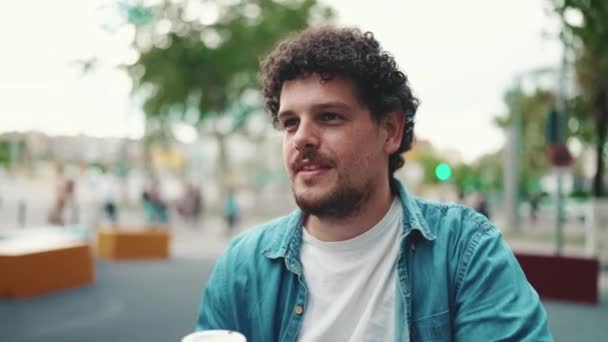 身着斜纹棉布衬衫的年轻大胡子男子坐在繁忙的街道现代城市背景下喝咖啡的特写 喝咖啡的人的概况 — 图库视频影像