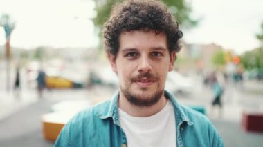 Kot gömlekli sakallı genç adamın ön yakın plan portresi modern şehir arka planında kameraya poz veriyor ve gülümsüyor..