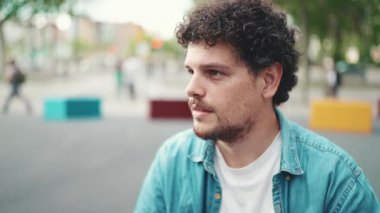 Kot gömlekli genç sakallı adamın yakın plan portresi başını çevirip modern şehir arka planında kameraya gülümsüyor.
