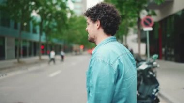 Kot gömlekli genç sakallı adamın modern şehir arka planında yaya geçidinden geçerken gülümsemesi.