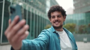 Yakın plan, genç sakallı adam akış yapıyor, modern binalar için video çağrısı yapıyor.