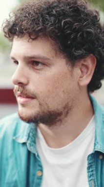 Kot gömlekli sakallı genç adamın yakın plan portresi başını çeviriyor ve modern şehir arka planında kameraya gülümsüyor.