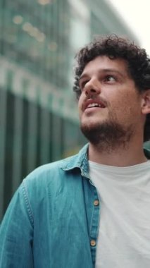 Yakından bakınca, kot gömlekli adam caddede yürüyor, duruyor ve modern binaların üst katlarına bakıyor.