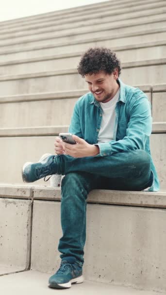 Glimlachende Jonge Man Met Baard Denim Shirt Zittend Hoge Treden — Stockvideo