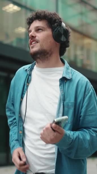 Emotionele Jonge Bebaarde Man Denim Shirt Loopt Door Straat Koptelefoon — Stockvideo