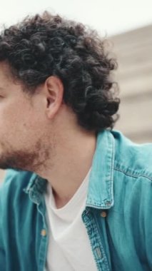 Sinirli bir adam merdivenlerde oturur ve duygusal olarak düşünür, tamam mı? Kot gömlekli duygusal sakallı genç adamın yakın plan portresi yüksek basamaklarda oturuyor..