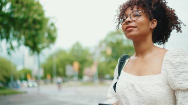 Gözlüklü genç bir kadın caddede yürüyor. Kız şehir arka planında sokağa çıkıyor