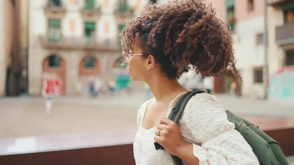 Young woman in glasses with a backpack walking on the downtown. Girl goes on the street in urban background