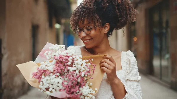 Young woman in glasses holding a bouquet of flowers on the street of the downtown. Girl with bouquet of flowers on the street on urban background