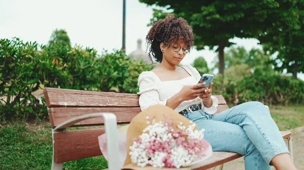 Jovem Mulher Senta Parque Banco Com Buquê Flores Com Smartphone — Fotografia de Stock
