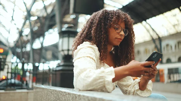 Gözlüklü Genç Bir Kadın Istasyonda Oturuyor Akıllı Telefona Bakıyor Gülümsüyor — Stok fotoğraf