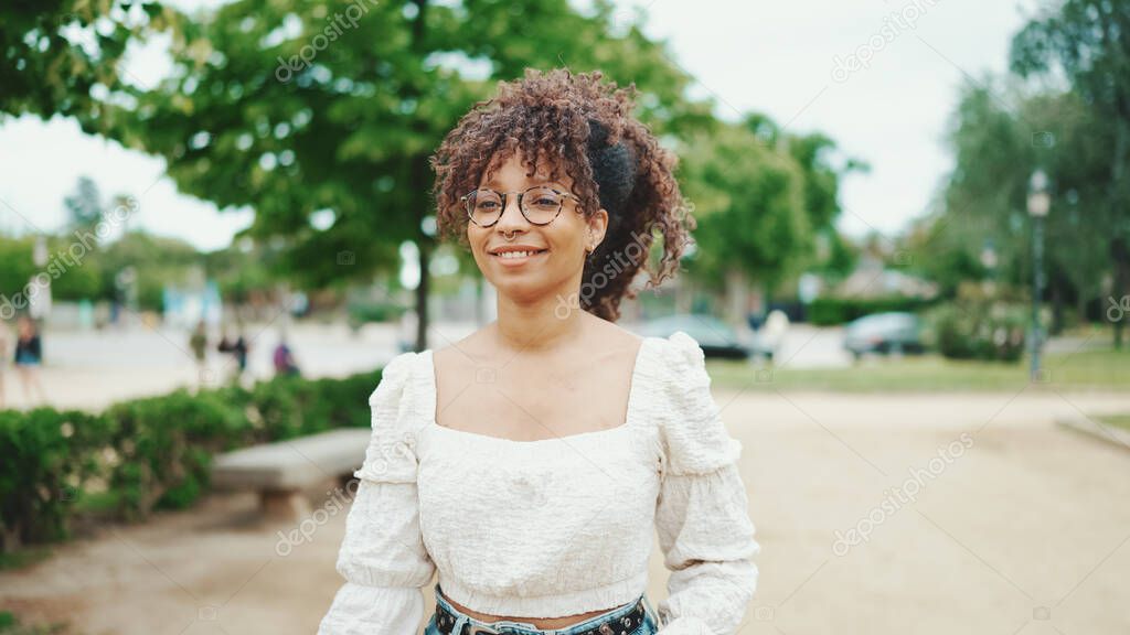 Smiling young woman walking in the park. Girl goes in the city park and looks at around