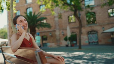 Şirin genç bir bayan sokakta cep telefonu kullanıyor. Kız eski şehrin arka planında bir bankta oturuyor ve akıllı bir telefonla konuşuyor.