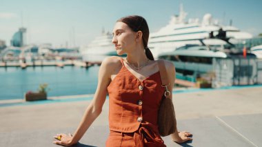 Deniz limanında kameraya poz veren gülümseyen kadın. Kız, yat ve gemilerin arka planında güneşli bir günün tadını çıkarıyor.
