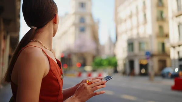 Close-up smiling young woman stands and looks at a map on a mobile phone. Girl stands on the street of the downtown scrolls the map on the smartphone.