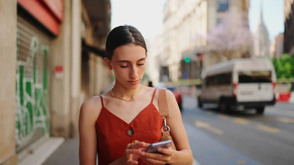 Close-up smiling young woman stands and looks at a map on a mobile phone. Girl stands on the street of the downtown scrolls the map on the smartphone.