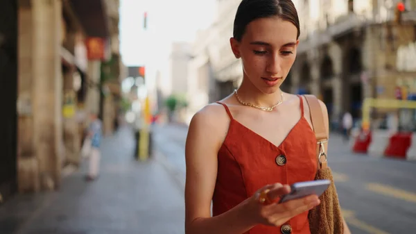 Close-up smiling young woman stands and looks at a map on a mobile phone. Girl stands on the street of the downtown scrolls the map on the smartphone.