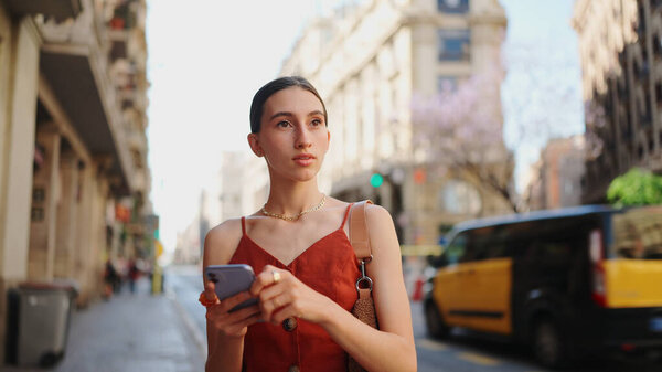 Крупным планом улыбающаяся молодая женщина стоит и смотрит на карту по мобильному телефону. Девушка стоит на улице в центре города перемещает карту на смартфоне.