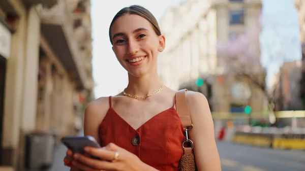 Close-up smiling young woman stands and looks at a map on a mobile phone. Girl stands on the street of the downtown scrolls the map on the smartphone.