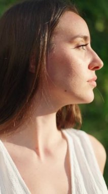 Çilli, koyu renk saçlı, beyaz bluzlu ve kot pantolonlu genç bir kadın etrafa bakıyor. Uzun kirpikleri olan güzel bir kız etrafına bakar ve başını kameraya çevirir.