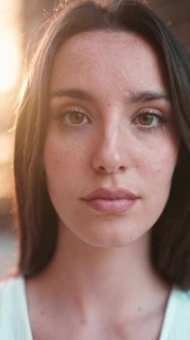 Çilli, koyu renk saçlı ve uzun kirpikli kameraya doğru bakan genç bir kadının yakın çekimi. Modern şehir geçmişinde güzel bir kız.