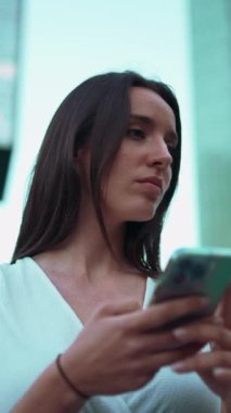 Çilli, koyu renk saçlı, beyaz bluzlu güzel bir kadın cep telefonundan haritaya bakıyor. Güzel kız yerini belirlemek için akıllı telefon kullanıyor.