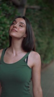 Yeşil bluzlu bir kız yol boyunca yeşil bitkilerle kaplı bir kemerin içinden geçiyor. Gülümseyen genç bir kadın yeşil yapraklarla kaplı duvara bakarak kaldırımda yürüyor.