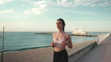 Saçı örülü, bej rengi spor giyinen genç atletik bir kadın.