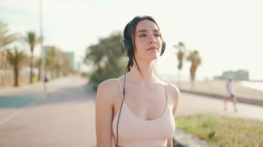 Örgülü at kuyruklu, kulaklıklı, bej rengi spor tişörtlü genç atletik kadın setten aşağı doğru yürüyor. Müzikten hoşlanan güzel kız. Kamera hareket ediyor