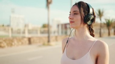 Saçları örgülü, bej renkli, kulaklık takan, setin üzerinde duran atletik bir kadın. Güzel kız elini çapraz yapar ve kameraya gülümser.