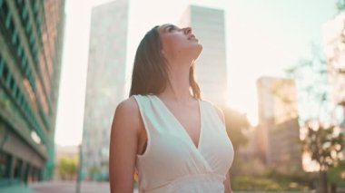 Çilli, koyu renk saçlı, beyaz bluzlu ve kot pantolonlu hoş bir bayan modern şehir manzarasının tadını çıkarıyor. Uzun kirpikleri olan güzel bir kız binanın üst katlarına bakıyor.