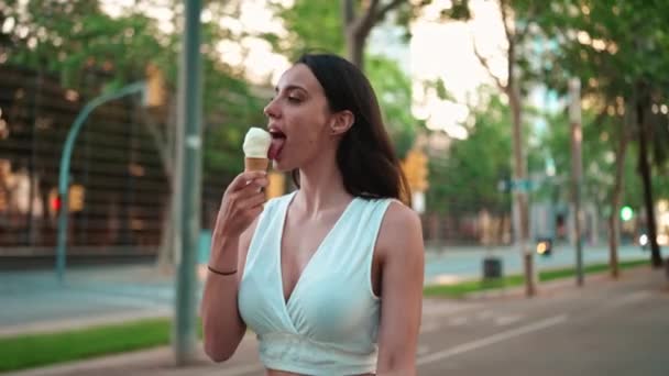 身穿白色上衣 长着雀斑和乌黑蓬松的头发的漂亮女人正在街上散步 试吃着冰淇淋 可爱的女孩喜欢现代都市背景的冰淇淋 — 图库视频影像