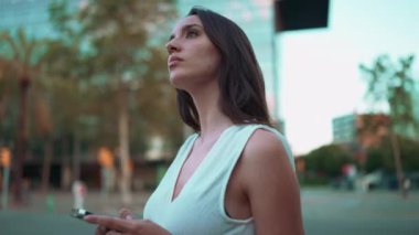 Çilli, siyah saçlı, beyaz bluzlu güzel bir kadın cep telefonundan haritaya bakıyor. Güzel kız yerini belirlemek için akıllı telefon kullanıyor. Kamera dönüyor.
