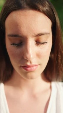 Çilli, koyu renk saçlı, beyaz bluzlu ve kot pantolonlu genç bir kadın gözlerini açıyor ve gülümsüyor. Uzun kirpikleri olan güzel bir kız kameraya gülümsüyor.