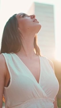 Çilli, koyu renk saçlı, beyaz bluzlu ve kot pantolonlu hoş bir genç kadın modern şehir manzarasının tadını çıkarıyor. Uzun kirpikleri olan güzel bir kız binanın üst katlarına bakıyor.