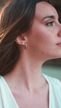 Yakın plan, çilli, koyu renk saçlı, beyaz bluzlu ve kot pantolonlu hoş bir genç kadın başka yere bakıyor. Modern şehir geçmişinde güzel bir kız.