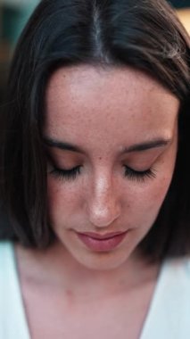 Çilli, koyu renk saçlı, beyaz bluzlu güzel bir kadın bankta oturur ve etrafına bakar. Şirin kız modern şehir geçmişinde oturuyor.