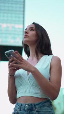 Çilli, koyu renk saçlı, beyaz bluzlu güzel bir kadın cep telefonundan haritaya bakıyor. Güzel kız yerini belirlemek için akıllı telefon kullanıyor.