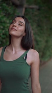 Yeşil bluzlu bir kız yol boyunca yeşil bitkilerle kaplı bir kemerin içinden geçiyor. Gülümseyen genç bir kadın yeşil yapraklarla kaplı duvara bakarak kaldırımda yürüyor.