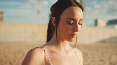 Uzun at kuyruklu, bej renkli spor bluzlu genç atletik kadın güneşin doğuşunda nefes alma egzersizleri yapıyor.