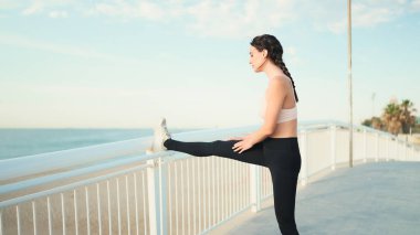 Örgülü at kuyruklu, bej rengi spor bluzlu genç atletik kadın, arka planda koştuktan sonra vücudunu esnetiyor.