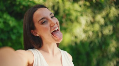 Çilli, koyu renk saçlı, beyaz bluzlu ve kot pantolonlu genç bir kadın akıllı telefondan selfie çekiyor. Kameralı cep telefonunda poz veren uzun kirpikli güzel bir kız.