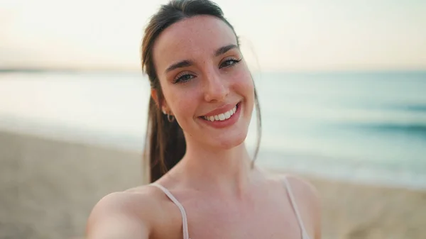 Uzun at kuyruklu, bej rengi spor tişörtlü genç atletik kadın gülümsüyor ve arka planda selfie çekiyor.