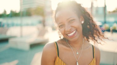 Kentin arka planında uzun kıvırcık saçlı, gülümseyen bir kadının yakın plan portresi. Saçı düzelten ve kameraya bakan mutlu kızın önden yakın çekimi.