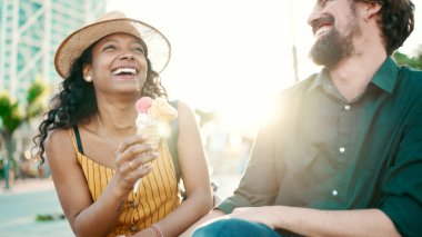 Şehirdeki arka planda dondurma yiyen mutlu ırklar arası çiftin yakın plan portresi. Kadın ve erkeğin dondurma tattığı yakın çekim. Arkaplan