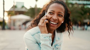 Kentin arka planında cep telefonu kullanan uzun kıvırcık saçlı genç bir kadın. Akıllı telefondan konuşan bir kızın yakın çekimi.