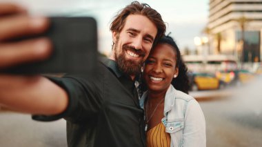Gülümseyen ırklar arası çiftin fıskiyenin arka planında selfie çekmesi. Yakın plan, erkek ve kadın cep telefonu kullanarak görüntülü sohbet.