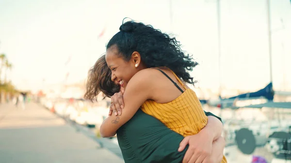 Closeup, happy meeting of young interracial couple. Young man and woman joyfully embrace when they meet on the embankment on the yacht background. Camera moves around people