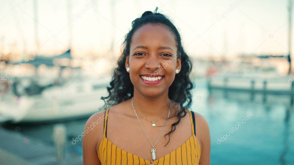 Close-up portrait of smiling girl with long curly hair on the embankment, on yacht background. Frontal closeup of happy young woman looking at camera