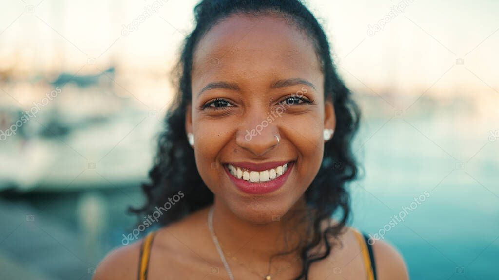 Close-up portrait of smiling girl with long curly hair on the embankment, on yacht background. Frontal closeup of happy young woman looking at camera